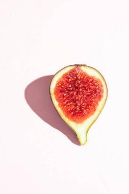 Tek bir yarım kesilmiş incir, pembe bir tabağın üzerine, yumuşak pembe bir arka plana yerleştirilmiş parlak kırmızı iç yüzeyini ortaya çıkarır. Taze ve çarpıcı.