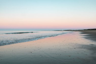 Playa de los Enebrales, Huelva, güneşin doğuşunda büyüleyici pembe gökyüzü ve turkuaz sularla yakalandı, rüya gibi bir sahil manzarası yarattı.