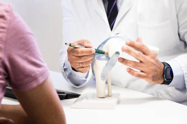 Doktor hastaya diz bağlarını bir model kullanarak öğretiyor, eklem yapısını ve yaralanmayı önlemeyi öğretiyor.