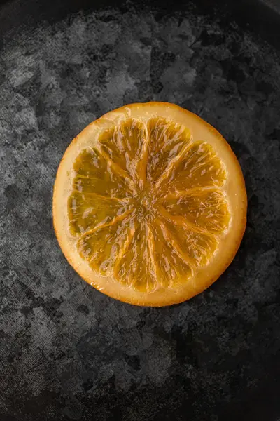 Tek bir parlak turuncu dilim, mükemmel karamelize edilmiş, koyu metalik bir yüzeye yerleştirilmiş, karmaşık detaylar ve canlı renkler sergiliyor.