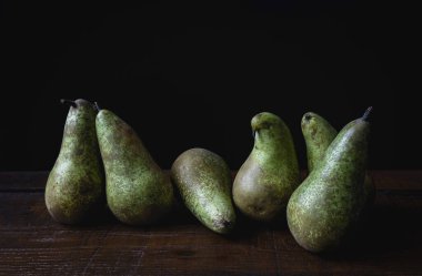 Altı olgun armut ahşap bir masaya dizilmiş, kırsal ve zarif bir görünüm için koyu bir zemin ile güzel bir tezat oluşturuyor.