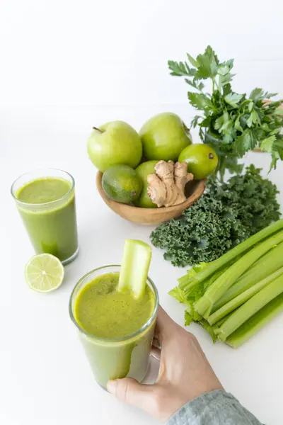 Yeşil detoks suyu, lahanadan, kerevizden, limondan, zencefilden ve yeşil elmadan yapılır. Beyaz mutfak tezgahına konur.