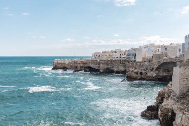 Polignano a Mare, Puglia sahilinin manzarası, beyaz binalar, kayalık kayalıklar ve güney İtalya 'nın berrak mavi sularını gösteriyor..