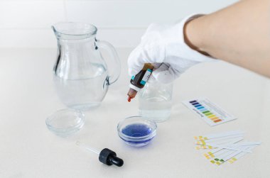 Renk göstergesi düşüşlerini de içeren bir su pH test kitinin fotoğrafları ve evde veya eğitim ortamlarında içme suyunun asitlik veya alkalikliğini analiz etmek için kullanılan bir karşılaştırma grafiği.