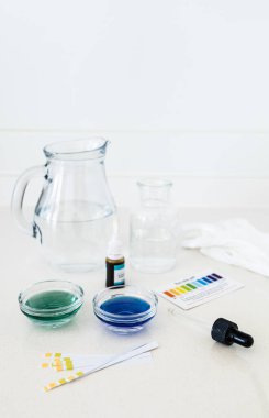 Renk göstergesi düşüşlerini de içeren bir su pH test kitinin fotoğrafları ve evde veya eğitim ortamlarında içme suyunun asitlik veya alkalikliğini analiz etmek için kullanılan bir karşılaştırma grafiği.