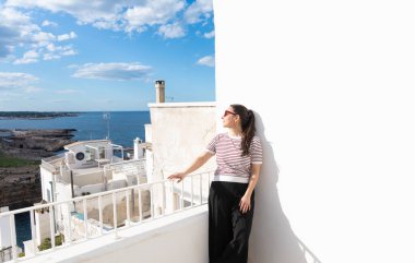 Polignano, Puglia 'da bir terasta duran bir kadın manzaralı kıyı şeridine ve beyazlatılmış binalara hayran.