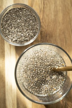 Kuru chia tohumlarının en üst görüntüsü bir kasenin içinde, bir bardak ıslak chia tohumunun yanında, doğal jellerini salıyor.