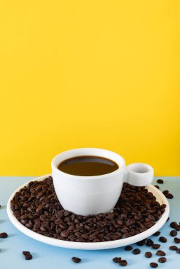 Sade kahve ve kavrulmuş fasulyelerle dolu beyaz seramik bir fincanın olduğu koyu renkli bir fonda stilize kahve sahnesi..