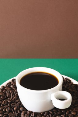 Süslü promosyon fotoğrafı. Beyaz bir seramik fincanda siyah kahve, kavrulmuş kahve çekirdekleri..