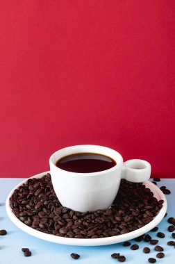 Sade kahve ve kavrulmuş fasulyelerle dolu beyaz seramik bir fincanın olduğu koyu renkli bir fonda stilize kahve sahnesi..