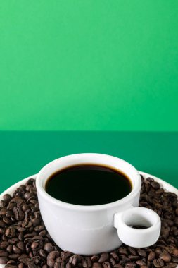 Süslü promosyon fotoğrafı. Beyaz bir seramik fincanda siyah kahve, kavrulmuş kahve çekirdekleri..