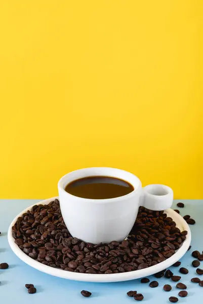 Sade kahve ve kavrulmuş fasulyelerle dolu beyaz seramik bir fincanın olduğu koyu renkli bir fonda stilize kahve sahnesi..