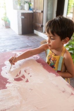 Yeşillik ve doğal ışıkla çevrili, evdeki bahçede resim yapmaktan hoşlanan küçük bir çocuk..