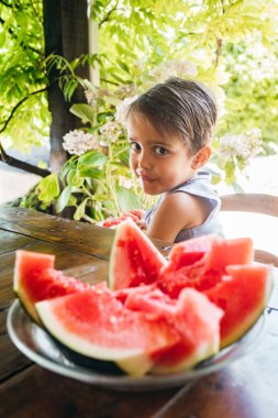 Çocuk kameraya bakarken sulu bir dilim kırmızı karpuz alıyor..