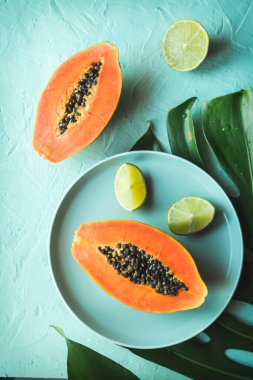 Büyük bir tropik yaprağın üzerine yerleştirilmiş taze limon ve yarıya kesilmiş olgun bir papayayı gösteren düz bir resim.
