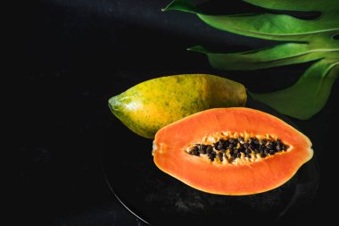 İkiye bölünmüş sulu, canlı bir papaya arkasında tropikal bir yaprak olan koyu bir arka plana yerleştirilir.