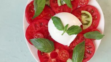 Canlı yeşil fesleğenli taze ve renkli mozzarella salatasını gösteren yakın plan bir video.