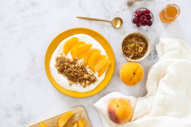 Yoğun Yunan yoğurdu, sulu şeftali dilimleri ve gevrek ev yapımı keto granola içeren sağlıklı bir glütensiz kahvaltı tabağı..
