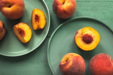 Lezzetli ve sulu kırmızı şeftaliler yeşil seramik tabaklarda aynı renkte pastel yeşil arka planda dizilmişler.