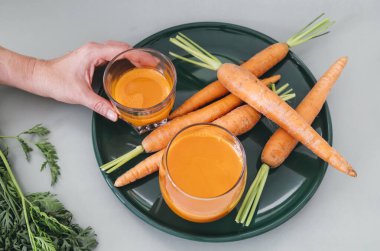 İçmeye hazır taze sıkılmış havuç suyuyla dolu iki temiz bardakla yeşil tabak..