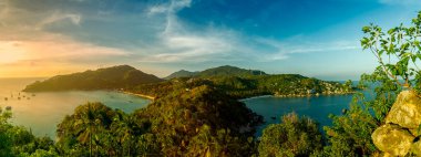 Tayland Körfezi 'ndeki Ko Tao Adası' nın en yüksek tepesinden günbatımı ve panoramik çekim. Uzakta solda balıkçı tekneleri ve sağda küçük bir kasaba var. Güneş batmadan önce mavi gökyüzü.
