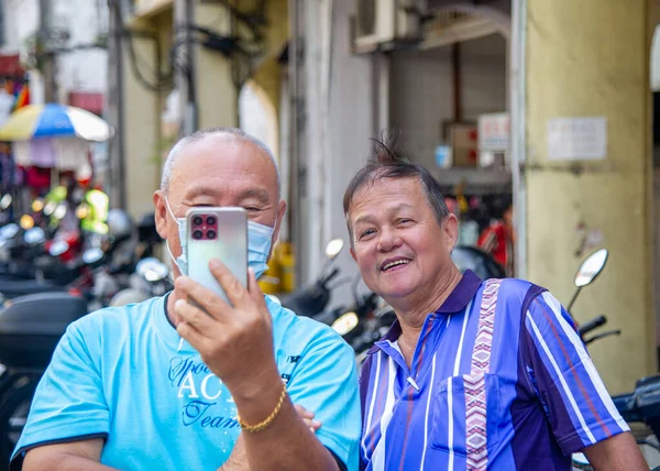 stock image February-21-2023- Penang-Malaysia- Two men in GorgeTown take pictures with their phones of tourists in a market, dressed in blue shirts