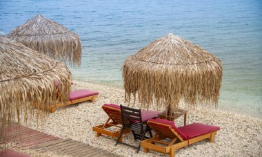 Yunanistan 'da saman şemsiyeleri ve mavi suya çok yakın kırmızı güneş pansiyonları olan güzel manzaralı bir plaj.