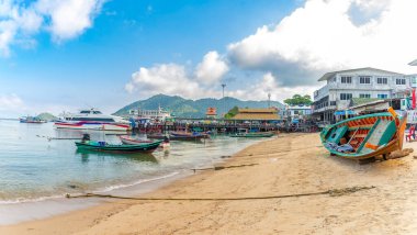 12 Mart 2023 - Ko Tao Tayland - Turistleri taşımak için parlak renkli Tayland tekneleri suda ve plajda oturur ve arka planda bekleyen turistlerle dolu dubayı görebilirsiniz .