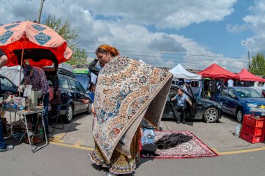 5 Ekim - 2023 Bükreş Romanyası. Her şeyi çok düşük fiyatlarla bulabileceğiniz bir bit pazarı. Bir kadın halı satmak istiyor ve onu omuzunda taşıyor..