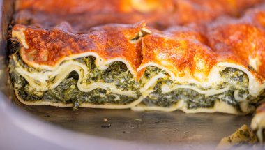 Soslu lazanya ve ıspanak. Bir tepside yakın plan çekimle yapılmış.