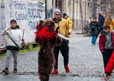 2 Aralık 2022 Bükreşli Romanya 'lı Noel şarkıcıları, sokakta ayı kürkü giymiş büyük kırmızı püsküllü bir meslektaşlarıyla şarkı söylerken hiç durmadan dans ediyorlar..