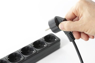 hand connects the plug to the outlet of the surge protector, The concept of starting an electrical device, saving electricity, on isolated white