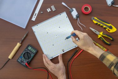 Aletleri olan bir masanın üst görünümü, bir elektrik teknisyeni bir LED lambayı tamir ediyor, yakın plan