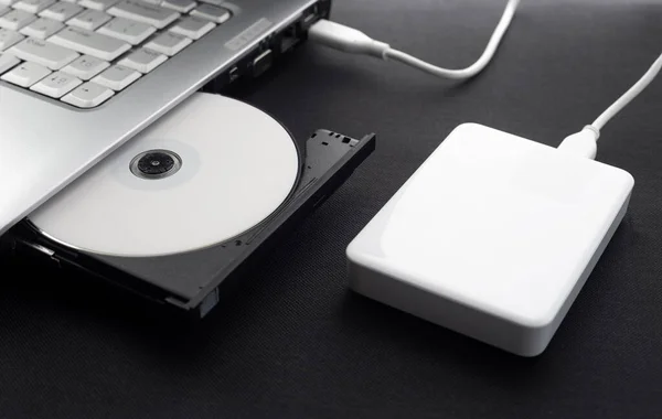 external hard drive connected to a laptop, open optical drive of a laptop with a disk, protected data, Data storage concept, on a dark background