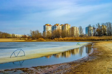 Melting ice on the beach on Dnieper river in Cherkasy city, Ukraine at sunny spring day. Residential buildings mirrored in melt-water
