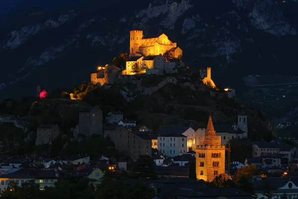 Geceleri Sion 'un büyüleyici atmosferi Valere Bazilikası' nın aydınlık güzelliği ve gece yarısı Notre Dame Katedrali 'nin görkemli kulesi. Sion, Valais Kantonu, İsviçre