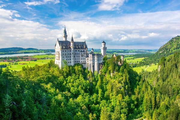 Захватывающее изображение замка Нойшванштайн, знакового немецкого сказочного замка. Белые стены и башенки замка на фоне пышной зелени создают потрясающий вид