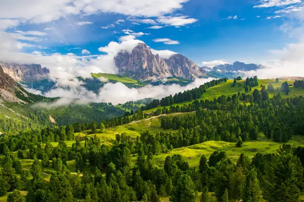 stock image A vibrant depiction of the Sassolungo Massif and Gardena Valley in Dolomite Alps, Italy. The foreground showcases a lush green valley, while the background highlights a cloud-covered mountain peaks