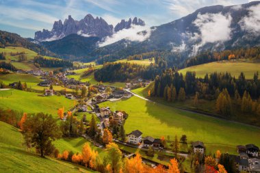 İtalya 'nın Dolomite Alpleri' nin Funes Vadisi 'nde yuva yapmış tuhaf Santa Maddalena köyünün büyüleyici bir görüntüsü. Huzurlu montaj manzarası yeşil tarlalar ve sonbahar renkli ağaçlarla süslenir.