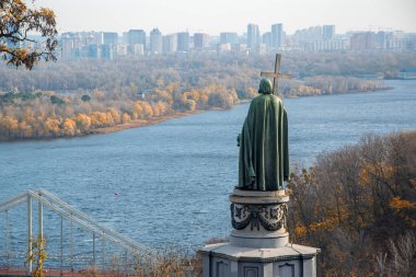 Sonbaharda Dinyeper Nehri ve Kyiv şehir manzarasına bakan Büyük Aziz Vladimir Heykeli. Anıt, şehir binaları ve renkli yapraklardan oluşan bir zemin üzerinde duruyor. Kyiv, Ukrayna