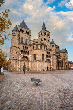 Bulutlu bir gökyüzüne karşı Trier Katedrali 'nin Roma mimarisi. Öndeki kaldırım taşı kare, sonbahar yaprakları görünür. Trier, Almanya 'da tarihi eser