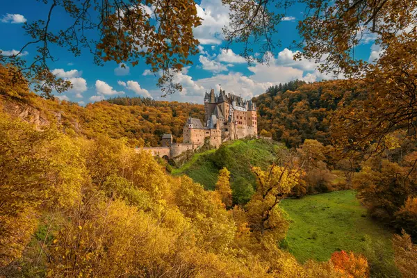 Majestic Burg Eltz kalesi Almanya 'nın Rhineland-Palatinate şehrinde canlı sonbahar yapraklarıyla çevrili. Mavi gökyüzünün altındaki altın ağaçlarla çevrili bir tepeye tünemiş ortaçağ kalesi..