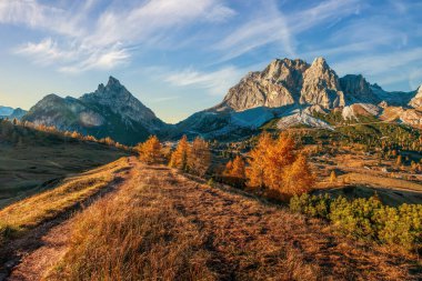 İtalya 'daki engebeli Dolomite dağlarının nefes kesici manzarası. Sonbaharın parlak altın ve yeşil yapraklarıyla zıt tepeler. Manzaralı bir yol dramatik manzaranın içinden geçiyor.