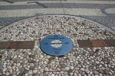 İtalya ile Slovenya arasındaki sınırı gösteren metal işaretli dairesel mozaik kaldırım, 1947-2004 yılları ve ülke isimlerini de içererek bölgedeki tarihi değişiklikleri sembolize ediyor.