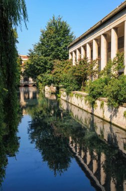 Vicenza 'daki sakin şehir kanalı. Tarihi binalar ve yemyeşil alanlar sakin sulara yansıyor. Sahne, İtalyan cazibesinin ve mimari güzelliğin özünü yakalıyor.