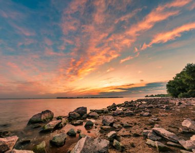 Kayalık sahilde muhteşem bir gün doğumu. Resimli bulutlar ve rengarenk su sabahları yansıyor.