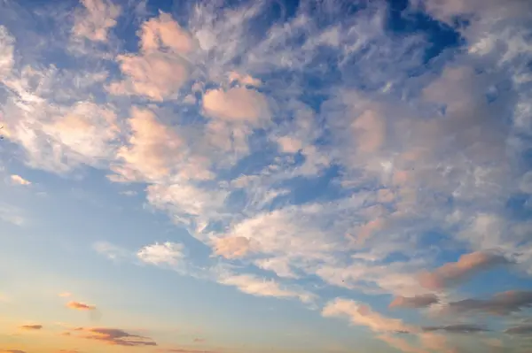A serene sunset sky filled with wispy clouds in soft pastel hues of pink, orange, and blue. The ethereal cloudscape creates a dreamy atmosphere as day transitions to evening