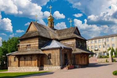 Traditional wooden Orthodox church with golden dome and crosses in Chortkiv, Ukraine. Featuring unique architectural style with multiple levels and a stone foundation, set against a blue sky with clouds clipart