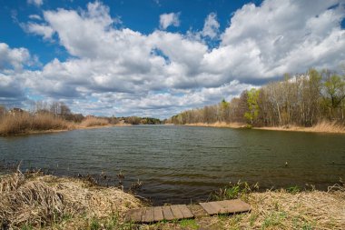 Dalgalı bulutlu bir gökyüzünün altında, tahta patikalı sakin bir göl sahnesi