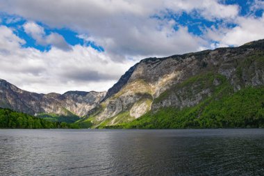 Dağlı Bohinj Gölü manzarası ve arka planda bulutlu gökyüzü, Slovenya 'nın güzel doğasını gözler önüne seriyor